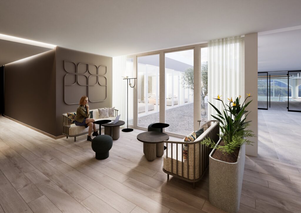 Eine Frau sitzt an einem kleinen Tisch in einer modernen Lounge mit hellem Holzfußboden, neutral getönten Möbeln und Zimmerpflanzen. Natürliches Licht erfüllt den Raum, während sie über einen Weinreise-Gutschein nachdenkt und durch große Fenster auf den einladenden Innenhof blickt.